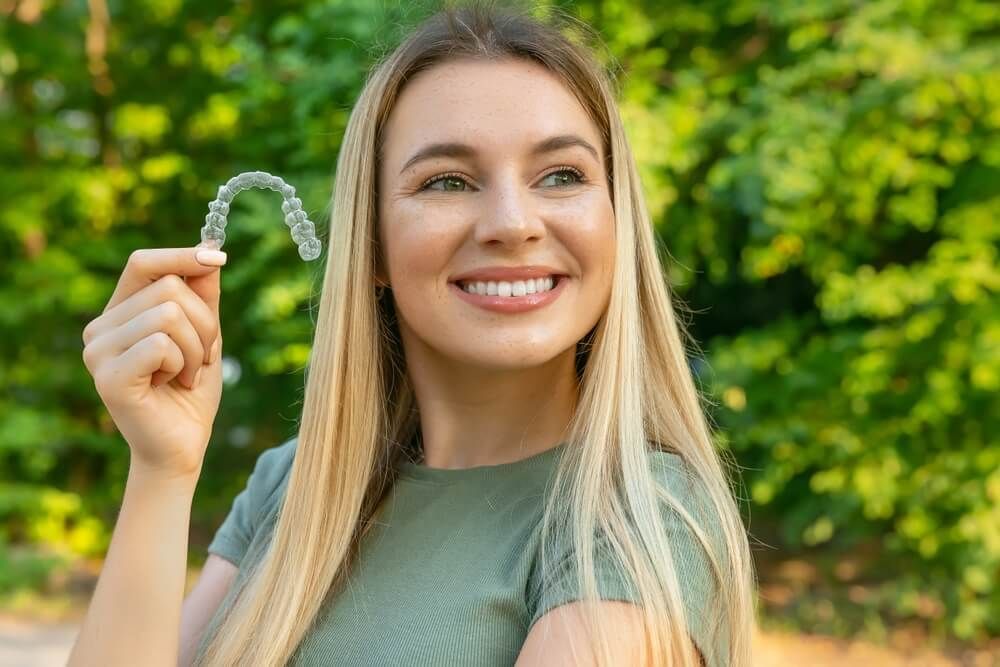 young beautiful woman smiling with hand holding dental aligner retainer (invisible)